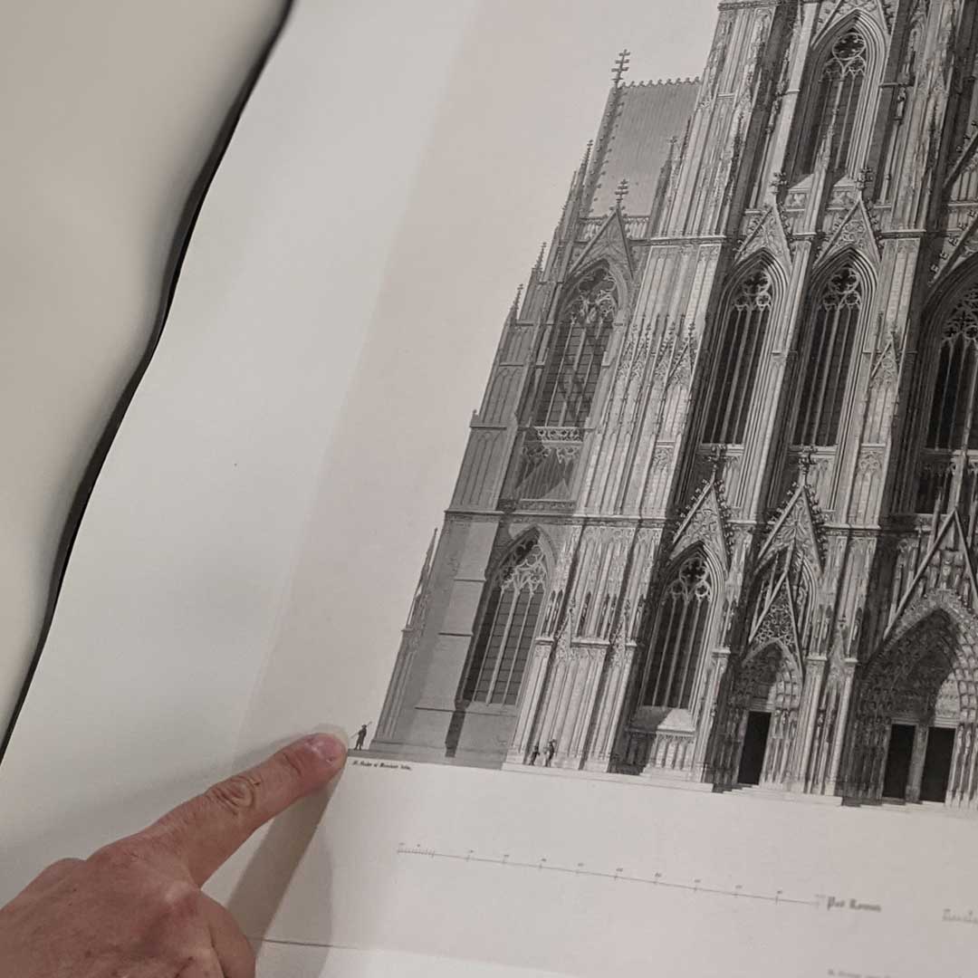 Ein Foto mit dem Ausschnitt einer Zeichnung des Kölner Doms. Dargestellt wird das Größenverhältnis von Mensch und Dom, dafür ist neben dem Gebäude eine kleine Figur abgebildet.