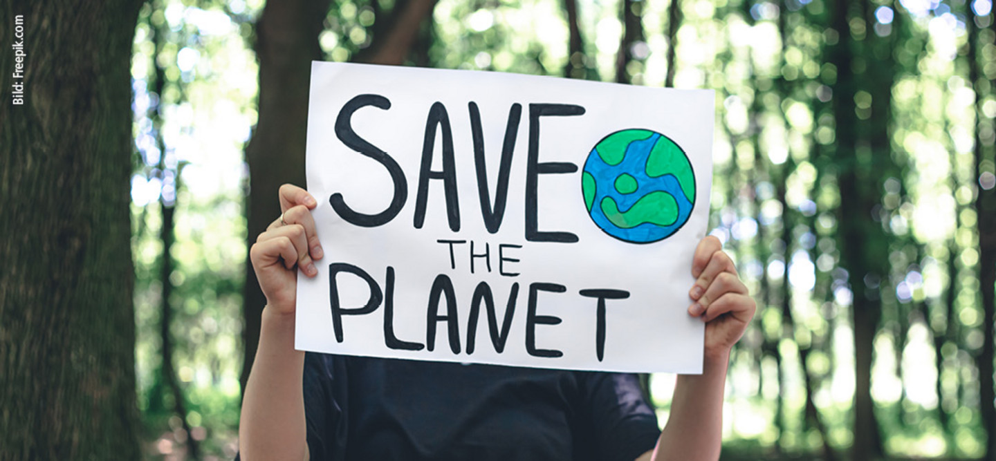 Mensch im Wald stehend hält Transparent hoch mit Schriftzug Save the planet