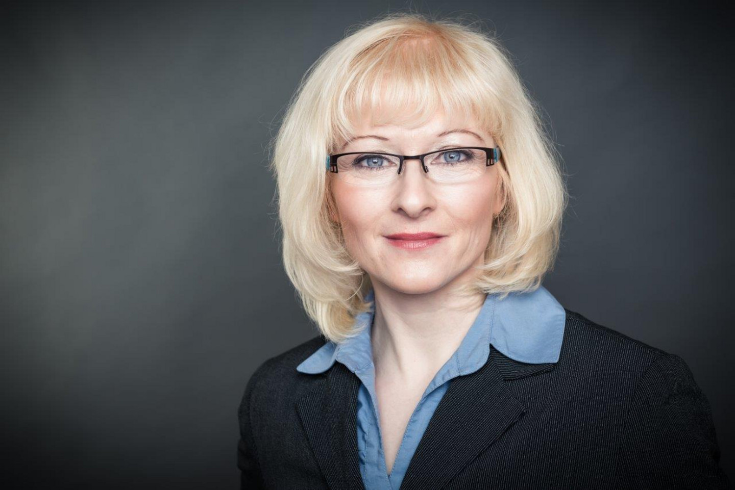 Porträt von Dr. Magdalena Spaude. Sie trägt eine Brille, hat blonde schulterlange Haare und trägt ein hellblaues Hemd.