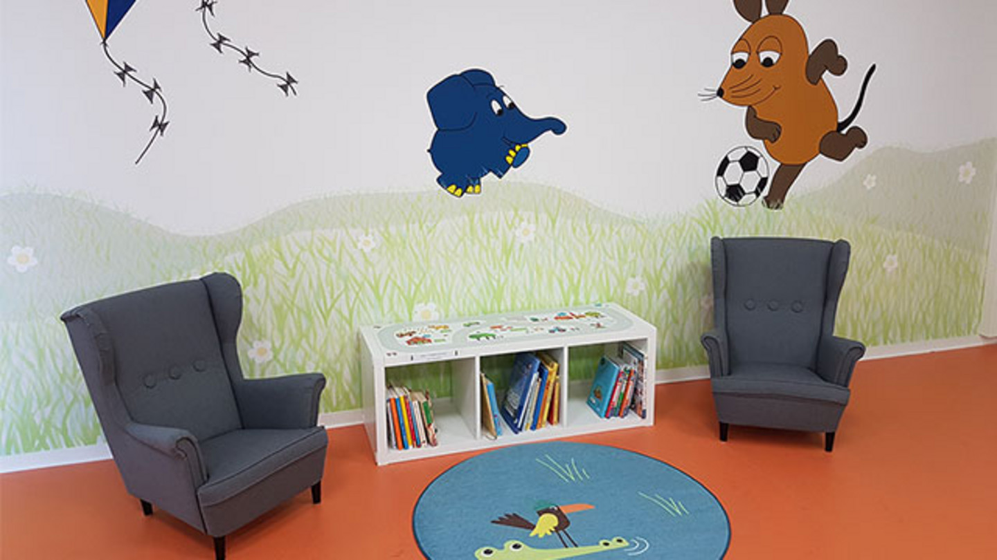 Two blue children's armchairs with bookshelf and colorful play rug
