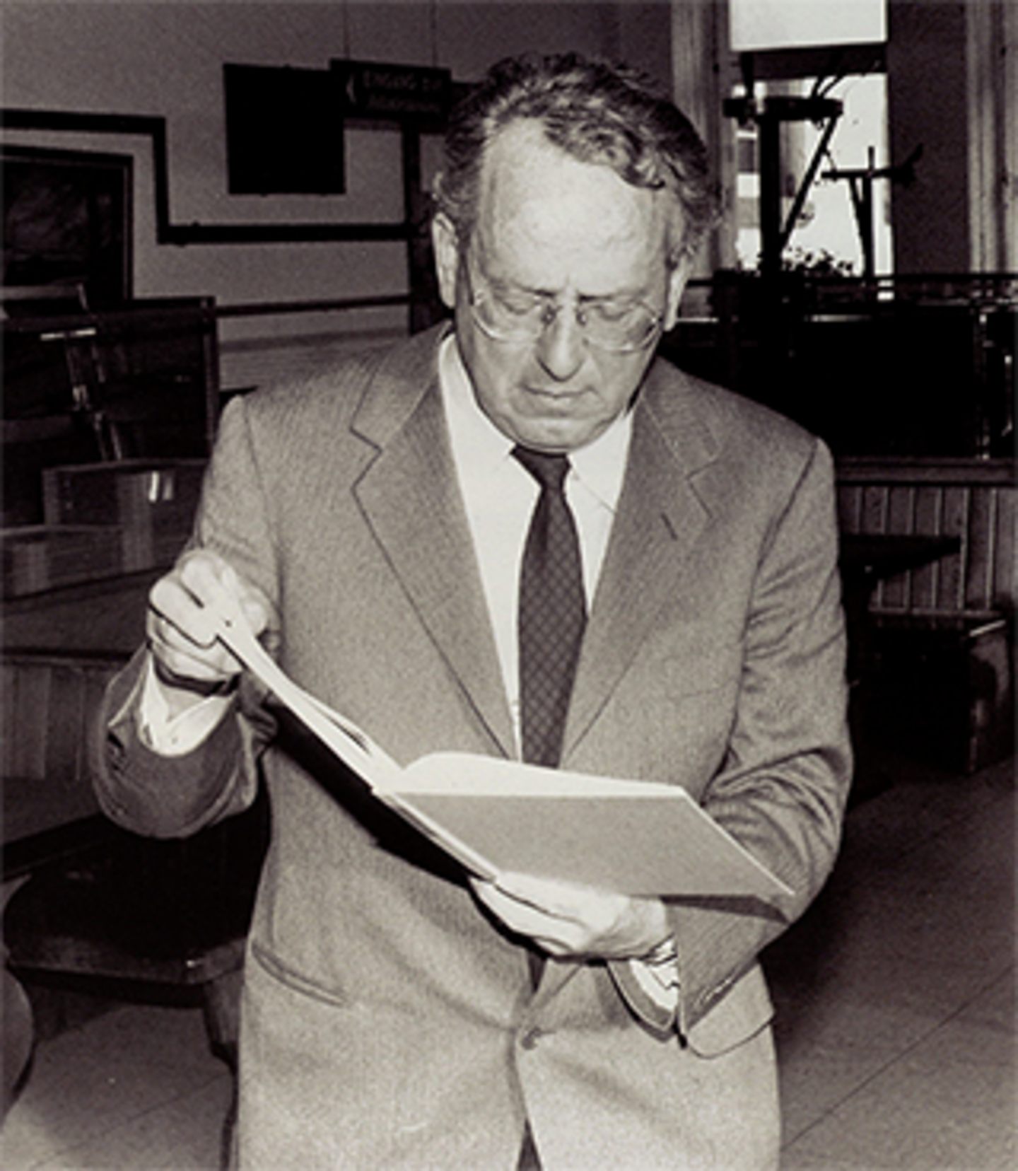 Ein Porträt von Georg Andreas Bachem im Jahr 1989. Er trägt einen Anzug und eine Brille, und hält ein offenes Buch in der Hand und richtet den Blick darauf.