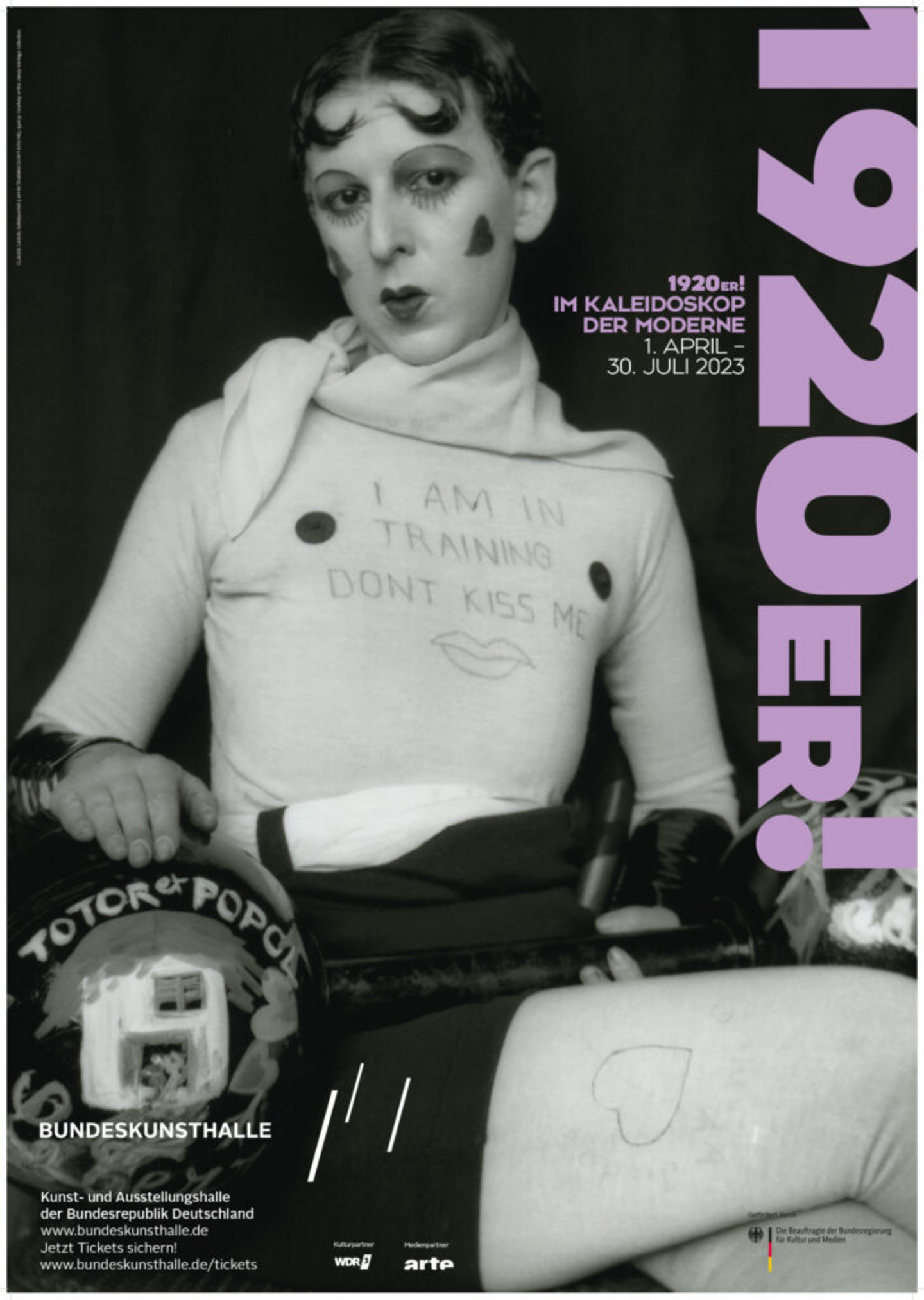 Schwarz-weißes Foto einer geschminkten Frau mit der Schrift "I am in training - don't kiss me" auf ihrem Oberteil.