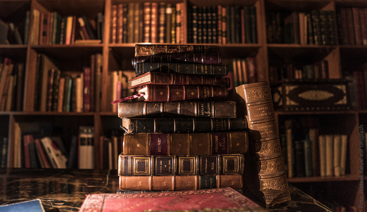 Wertvolle Bücher auf einem Tisch liegend vor einem Bücherregal