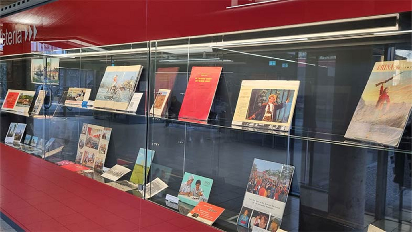 Das Foto zeigt einen rote Vitrine mit den Objekten der Ausstellung: Fotos, Zeitschriften, Flyer.