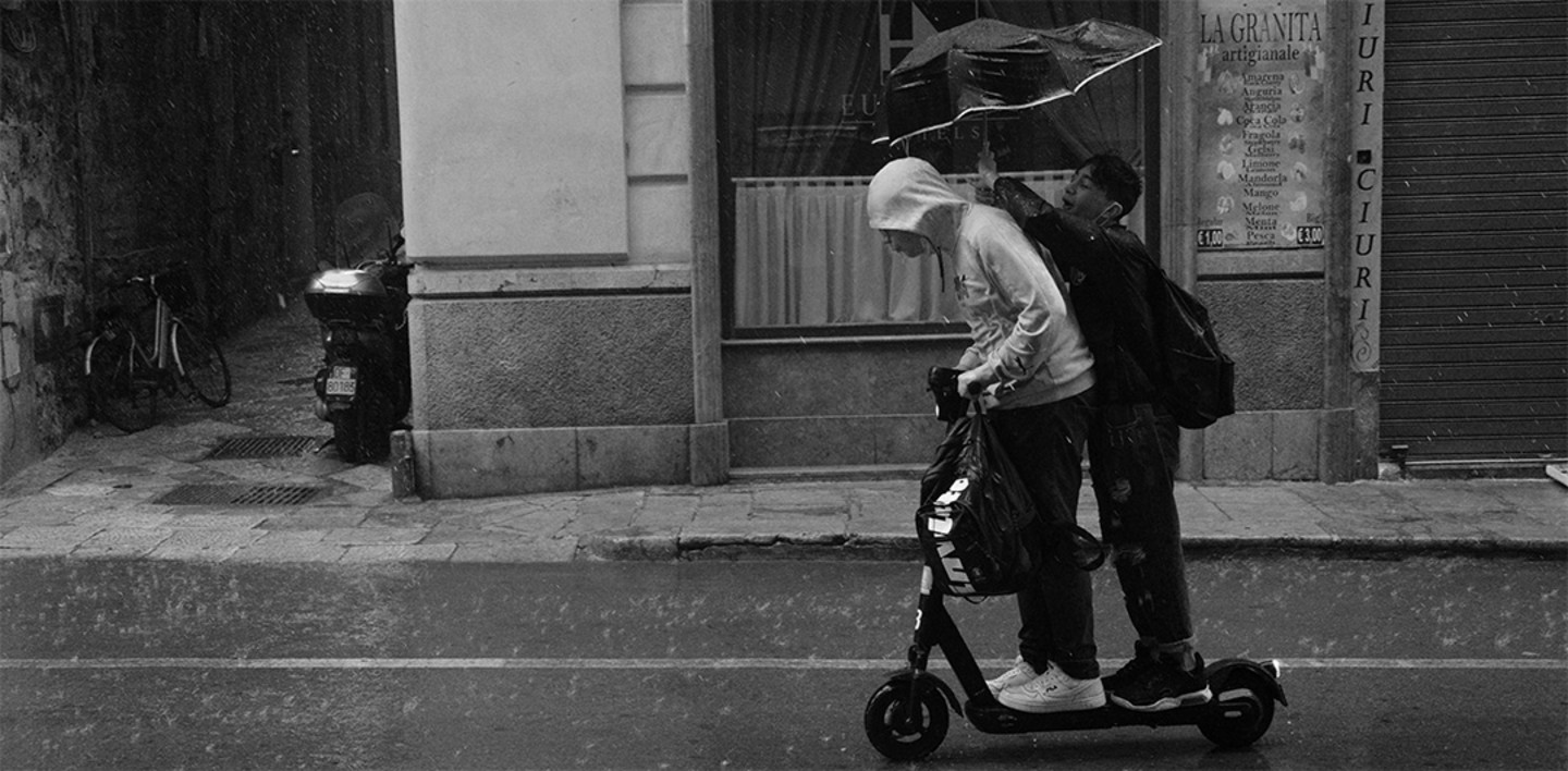 schwarz-weiß-Bild: zwei Jugendliche bei Regen auf einem gemeinsamen Roller fahrend