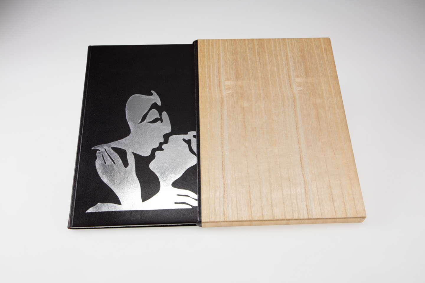 Das schwarze Buchcover steckt, halb verdeckt, in einem Buchschuber aus Holz.