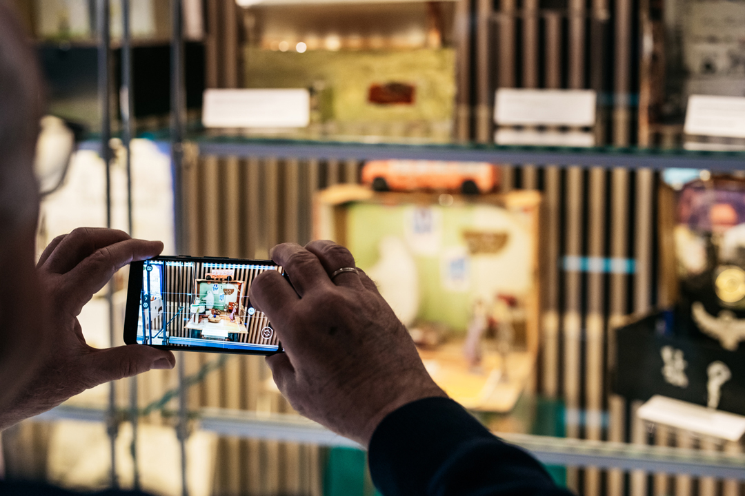 Ein Besucher fotografiert mit seinem Smartphone ein Exponat in einer Stehvitrine.